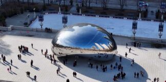 A large, reflective sculpture in a city park with people gathered around it