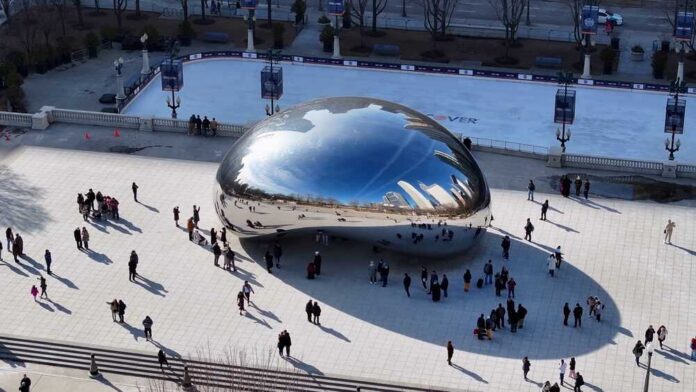 A large, reflective sculpture in a city park with people gathered around it