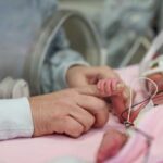A caregiver gently holding the hand of a premature baby in a hospital incubator