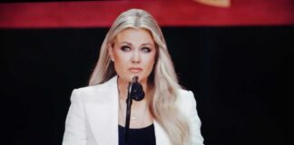 A woman in a white blazer speaking at a podium with a microphone
