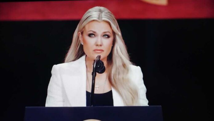 shutterstock_2682970915.jpg A woman in a white blazer speaking at a podium with a microphone