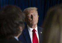 Easter Message: Trump Declares ‘America Needs God’ A serious-looking man in a suit with a red tie, surrounded by blurred figures