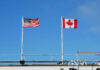 American and Canadian flags flying on poles against a clear blue sky