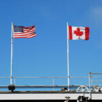 American and Canadian flags flying on poles against a clear blue sky
