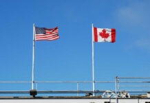 American and Canadian flags flying on poles against a clear blue sky