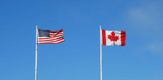 American and Canadian flags flying on poles against a clear blue sky