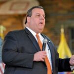 A man in a suit speaking into a microphone at an event