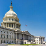 U.S. Capitol building with American flag, blue sky.