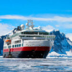 Ship navigating icy waters with snowy mountains behind