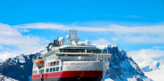 Ship navigating icy waters with snowy mountains behind