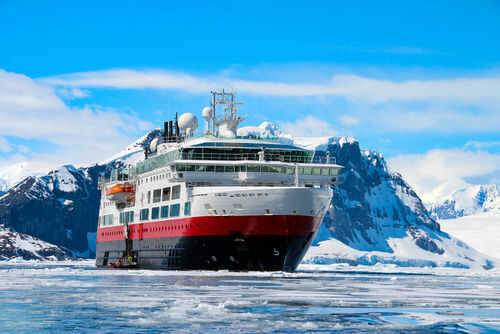 Ship navigating icy waters with snowy mountains behind