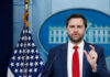 Man speaking at podium with US flag behind