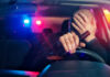 Driver holding beer bottle with police lights behind