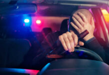 Driver holding beer bottle with police lights behind