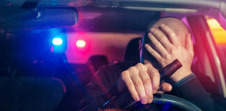 Driver holding beer bottle with police lights behind