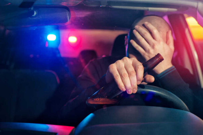male-driver-is-caught-driving-under-alcohol-influence535082599jpg Driver holding beer bottle with police lights behind