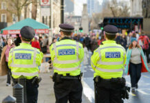 Three police officers in high-visibility jackets stand facing a busy street