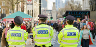 Three police officers in high-visibility jackets stand facing a busy street