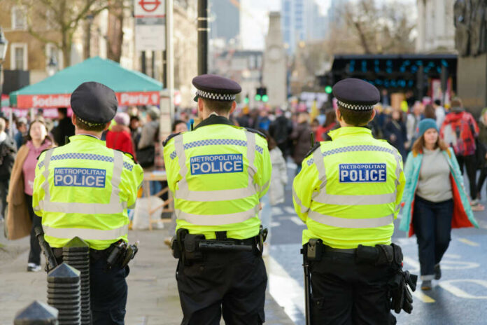 metropolitan-police2278725359jpg Three police officers in high-visibility jackets stand facing a busy street