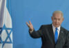 Man speaking next to Israeli flag.
