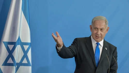 Man speaking next to Israeli flag.