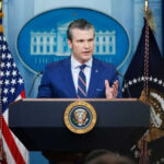 Memorial Day Uproar: Hegseth’s Bold Statement Stuns Man speaking at podium with flags in background