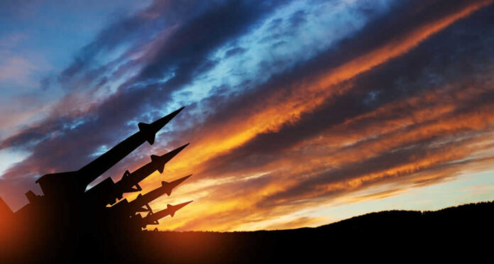 Silhouette of missiles against dramatic sunset sky.