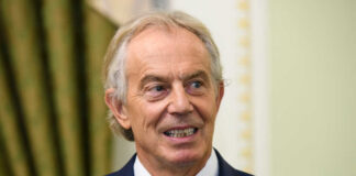 A smiling man in a suit with a blue tie, standing indoors