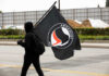 Individual in a black hoodie carrying an Antifascist flag during a protest