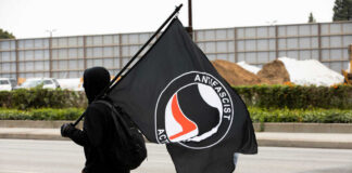 Individual in a black hoodie carrying an Antifascist flag during a protest