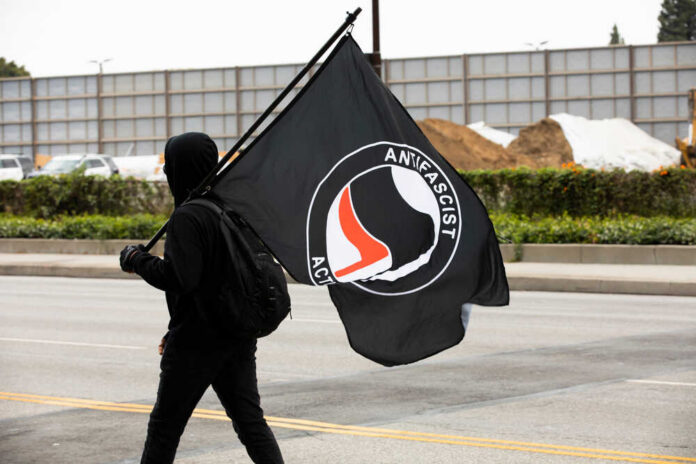 Individual in a black hoodie carrying an Antifascist flag during a protest