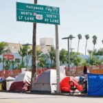 Homeless tents along a city street near a highway sign