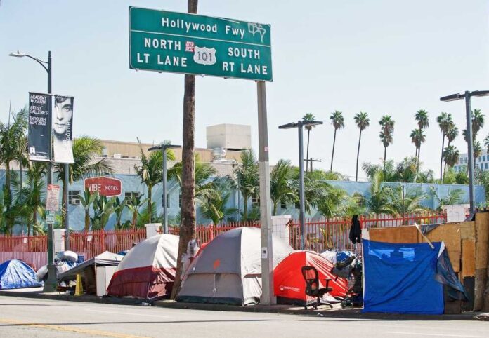 Homeless tents along a city street near a highway sign