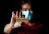 Person holding a wooden sign that reads 'LONG COVID' while wearing a mask
