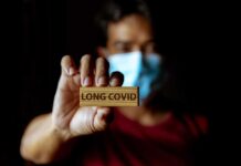Chewing Gum Cure for Long-Covid? Shocking Claim! Person holding a wooden sign that reads 'LONG COVID' while wearing a mask