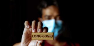 Person holding a wooden sign that reads 'LONG COVID' while wearing a mask