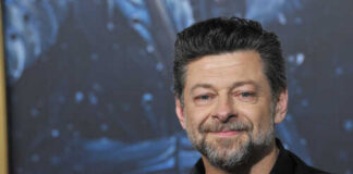 A smiling man in formal attire poses for a photo on the red carpet