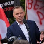 A speaker addressing a crowd at a political rally with flags in the background