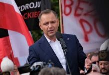 A speaker addressing a crowd at a political rally with flags in the background