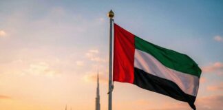 United Arab Emirates flag waving in front of a city skyline during sunset