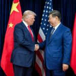 Two political leaders shaking hands in front of national flags