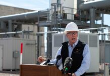 Man in a hard hat speaking at a podium in an industrial area