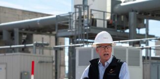 Man in a hard hat speaking at a podium in an industrial area