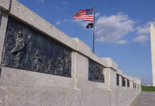 War memorial featuring bronze reliefs with soldiers and the Washington Monument in the background