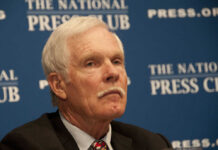 A man with gray hair and a mustache sitting at a press conference