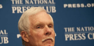 A man with gray hair and a mustache sitting at a press conference