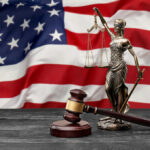 Lady Justice statue and judge’s gavel before a US flag