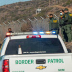 Northern Crossings Spike—What’s Getting Through? Border Patrol officers speaking with individuals near a fence.