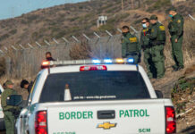 Border Patrol officers speaking with individuals near a fence.