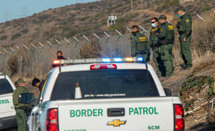 Border Patrol officers speaking with individuals near a fence.